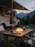 Husbil med utfälld markis och campingbord med boklampa i naturen – Smart Camping tillbehör för husbil och husvagn