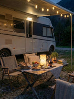 Husbil med markis och campingbord med boklampa på kvällen i naturen – Smart Camping tillbehör för husbil och husvagn