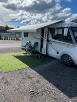 Vit husbil med utfälld markis och campingstolar på grusplan – perfekt campinguppställning för husbil och friluftsliv