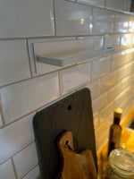 Tom väggmonterad hushållspappershållare mot vit kakelvägg med skärbrädor – köksorganisation för husbil och camping