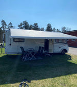 Vit husbil med stor markis fullt utfälld på grön gräsmatta under solig dag, campinglivsstil.