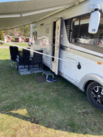 Sidan av en vit husbil med markisarm och entredörr, fotograferad vid camping i Sverige.