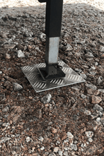 Stödbensplatta i metall med riffelmönster under stödben på grusunderlag – stabiliserar husbil och husvagn vid camping.