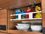Vit teleskopstång i träskåp med chips och skålar – effektiv kökförvaring i husbil och camping.