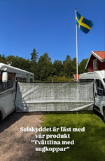 Husbil utomhus med tvättlina med sugkoppar fäst på sidan och solskydd på marken, svensk flagga i bakgrunden – camping.